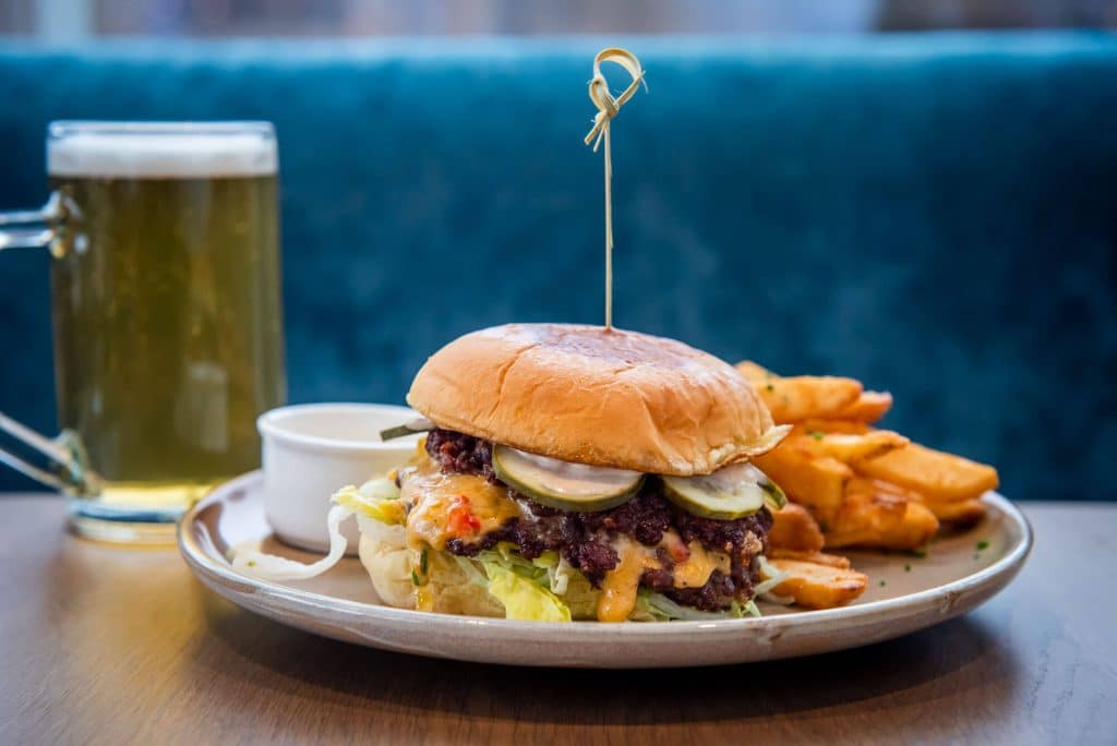 Salt + Ash's cheeseburger and fries on a dark table top with a glass of beer