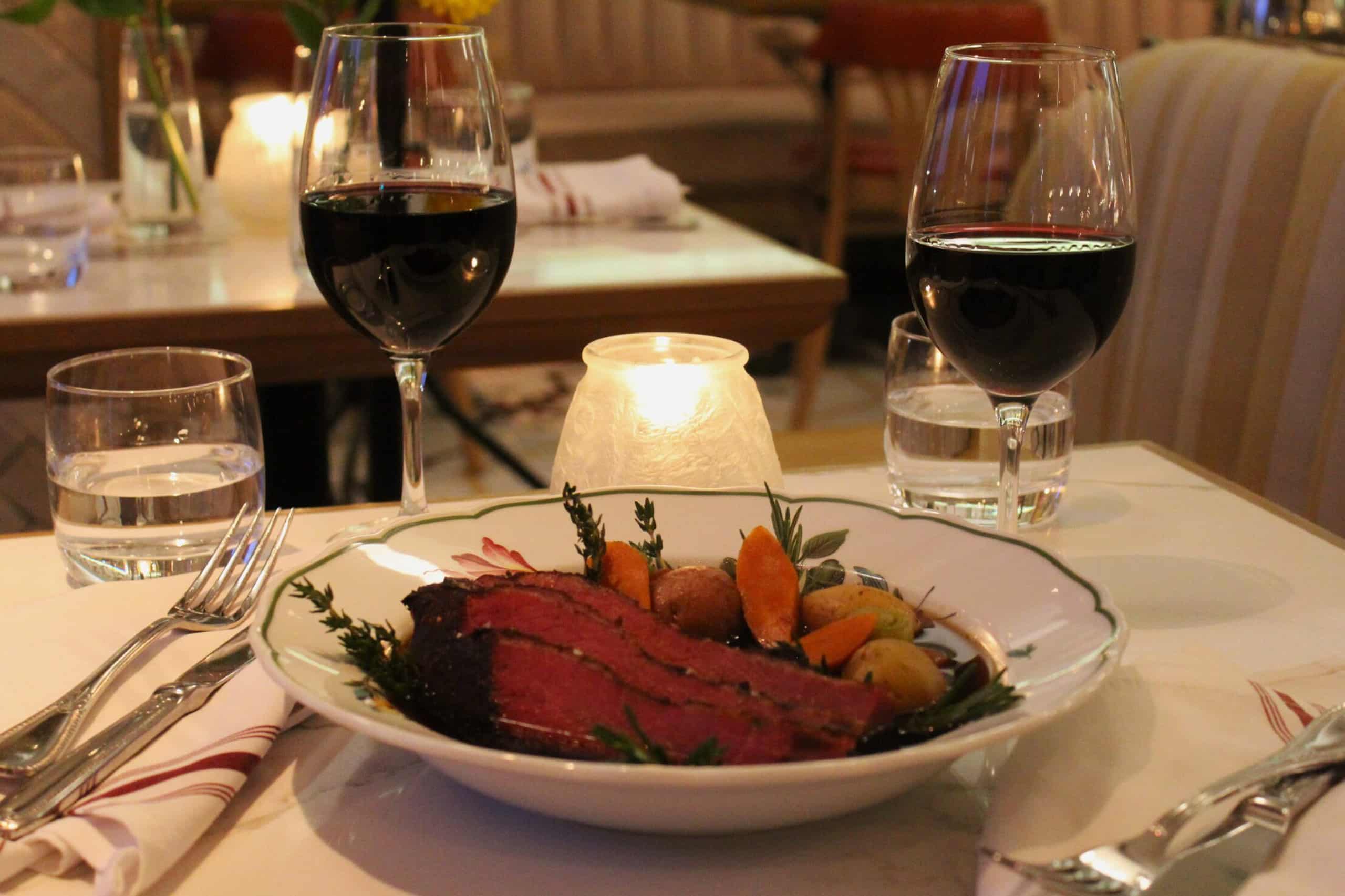 a table set for tow wit glasses of red wine and a meal