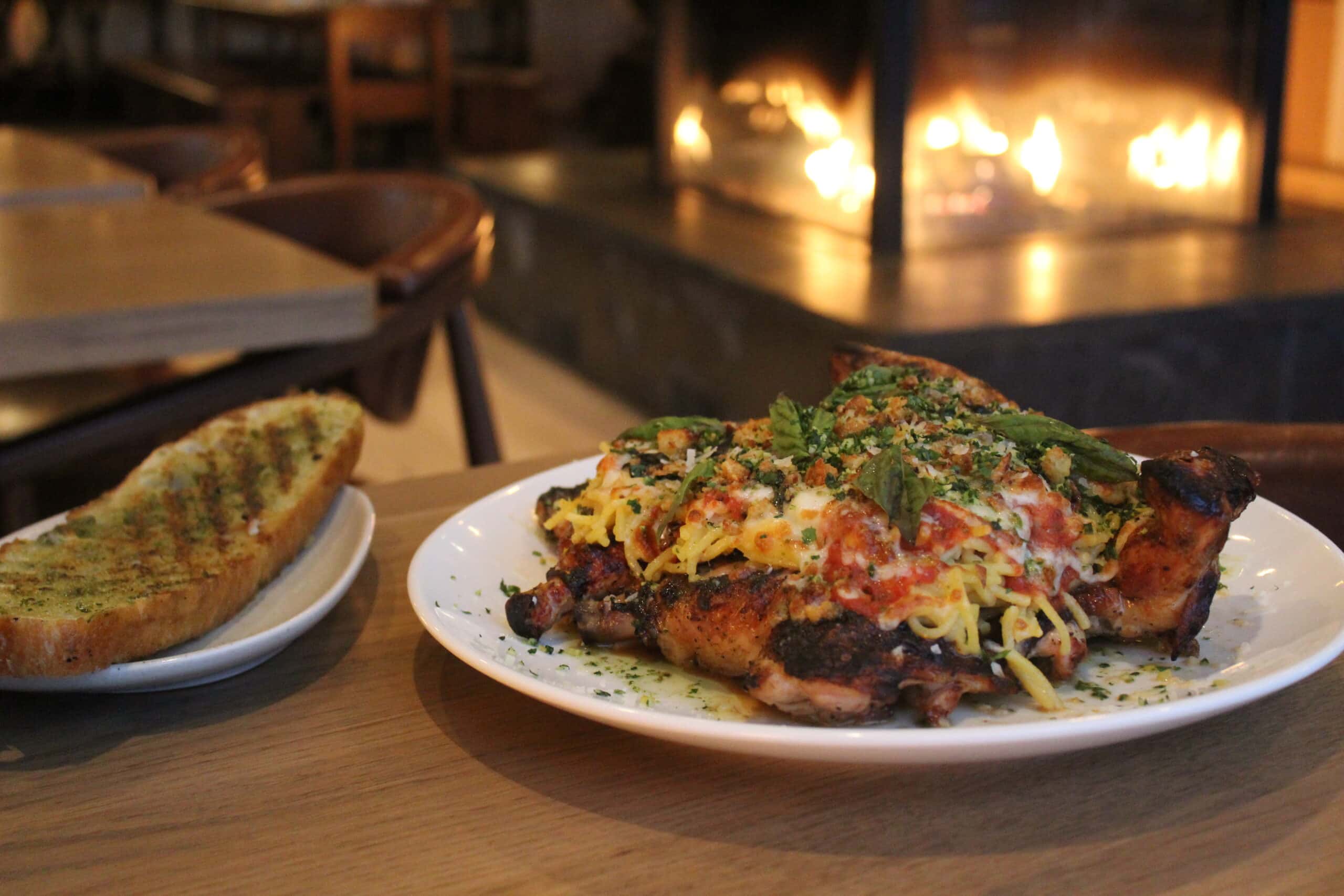 a meal on a wooden table sits in front of a well lit fireplace at Salt + Halifax